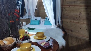 Una habitación acogedora con una cama, una mesa de comedor y productos para el desayuno, además de un tronco de árbol.