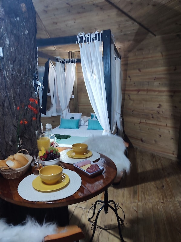 Una habitación acogedora con una cama, una mesa de comedor y productos para el desayuno, además de un tronco de árbol.