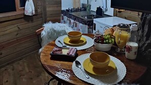 Interior acogedor de una cabaña de madera con una mesa de comedor lista para el desayuno, una zona de cocina y un televisor.