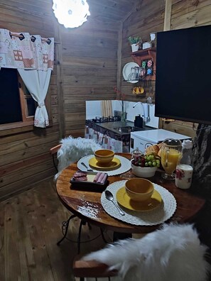 Interior acogedor de una cabaña de madera con una mesa de comedor lista para el desayuno, una zona de cocina y un televisor.
