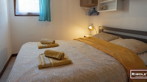 Un dormitorio con cama, lámpara de noche, espejo y ventana con cortinas.