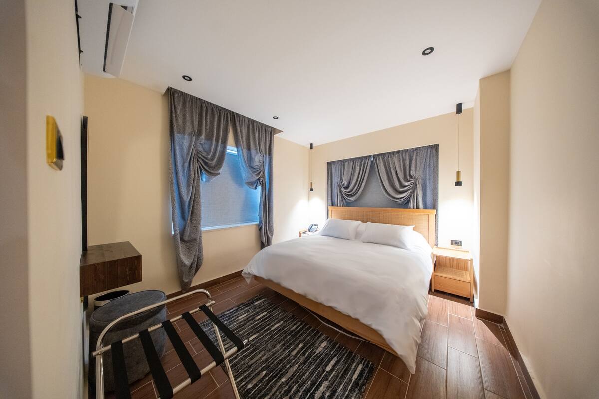 Une chambre d’hôtel avec un lit, une table de chevet, une lampe et une fenêtre avec des rideaux.