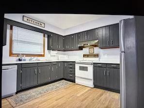 A kitchen with dark cabinets, a white refrigerator, and a window with blinds.