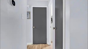 Un couloir avec une porte fermée, un interrupteur et un thermostat fixés au mur.