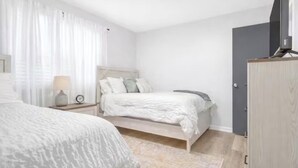 Une chambre avec deux lits, une table de chevet avec une lampe, une armoire et un téléviseur.