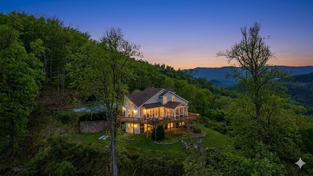 Une grande maison dotée d’une terrasse, entourée d’une forêt dense et de collines.