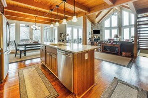 Une cuisine spacieuse avec un grand îlot central, des poutres en bois au plafond et une cheminée en pierre.