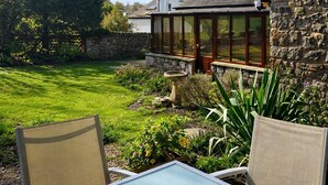 Une terrasse avec une table et des chaises, un mur en pierre et une maison avec un toit en pente et de grandes fenêtres.