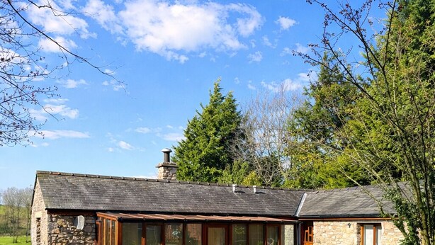Une charmante maison en pierre avec un toit en pente, de grandes fenêtres et une pelouse bien entretenue.