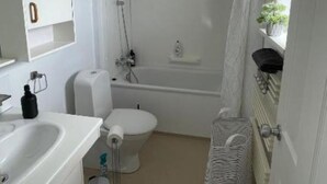 A compact, modern bathroom with a toilet, sink, shower, and a small window with a plant. - Quaint 3-bedroom apartment in charming Ásbrú neighborhood (Ásbrú)