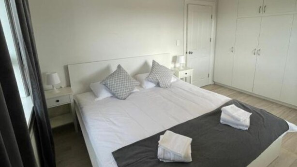 A bedroom with a large bed, white walls, a wardrobe, and a nightstand with a lamp. - Quaint 3-bedroom apartment in charming Ásbrú neighborhood (Ásbrú)