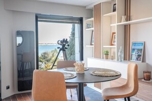 A modern dining area with a view of the sea, a tripod, and a bookshelf with a framed picture. - Villa pieds dans l'eau - vue mer & jacuzzi (Larmor-Plage)
