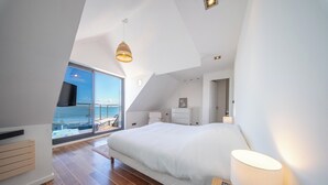 A bedroom with a large bed, a bedside table, a lamp, a TV, and a view of the sea through a large window. - Villa pieds dans l'eau - vue mer & jacuzzi (Larmor-Plage)
