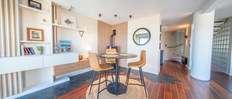 Un interior moderno con una mesa redonda para comer, dos sillas, un espejo fijado a la pared y una escalera.