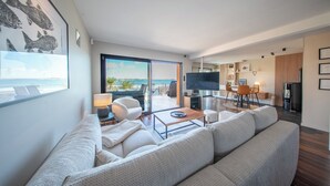 A modern living room with a sofa, coffee table, TV, and a view of the ocean through large windows. - Villa pieds dans l'eau - vue mer & jacuzzi (Larmor-Plage)
