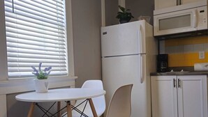 Kompakti keittiö, jossa on jääkaappi, mikroaaltouuni sekä pieni ruokailutila, jossa on pöytä ja tuolit.