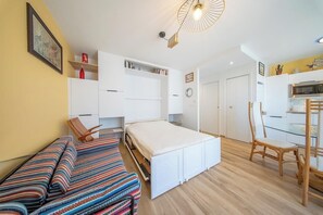Ein kleines Zimmer mit Bett, Sessel, Tisch und einer Küchenzeile.