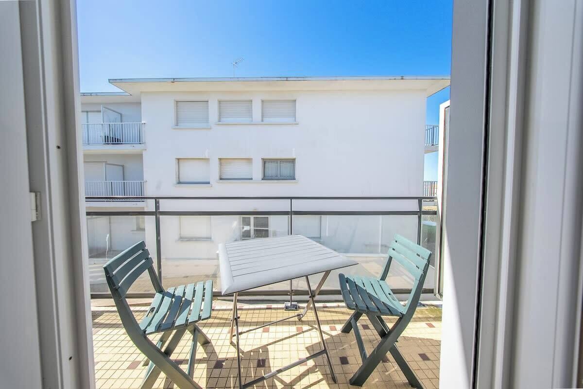 A balcony with a table and two chairs, a tiled floor, and a building with windows and balconies in the background.