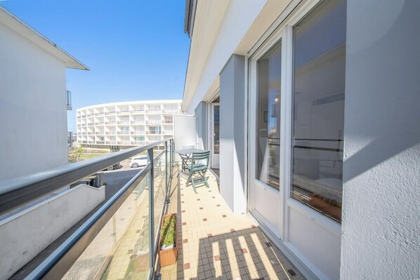 Ein Balkon mit Blick auf ein modernes Gebäude, ein kleiner Tisch mit Stühlen und ein Blumentopf.