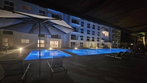 A swimming pool area with lounge chairs and umbrellas, surrounded by a building with multiple windows and balconies. - Stunning new Beachfront Condo 9th Floor Ocean View (Jacó)