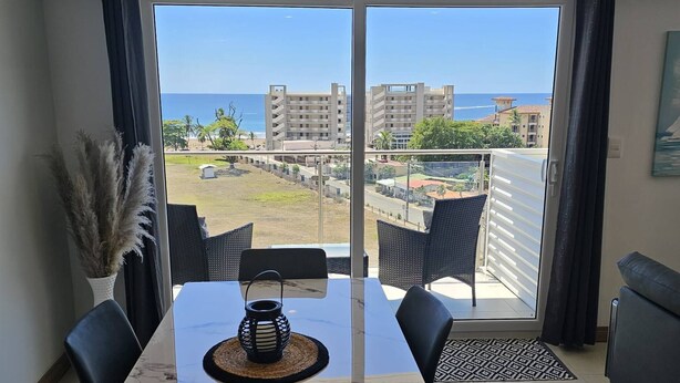 A dining area with a table, chairs, and a view of the ocean and buildings. - Stunning new Beachfront Condo 9th Floor Ocean View (Jacó)