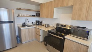 A modern kitchen with a stainless steel refrigerator, a black oven, a microwave, and wooden cabinets. - Stunning new Beachfront Condo 9th Floor Ocean View (Jacó)