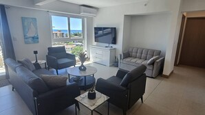 A modern living room with a sofa, armchairs, a coffee table, and a TV. - Stunning new Beachfront Condo 9th Floor Ocean View (Jacó)
