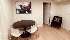 A dining area with a round table, white chairs, a colorful abstract painting, a door, and a patterned rug. - Basement Cozy Corner Be one of the first to stay in this comfortable space! (Salt Lake City)