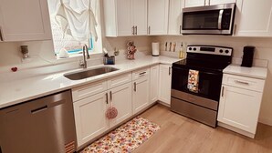 A modern kitchen with white cabinets, stainless steel appliances, a dishwasher, and a floral rug. - Basement Cozy Corner Be one of the first to stay in this comfortable space! (Salt Lake City)