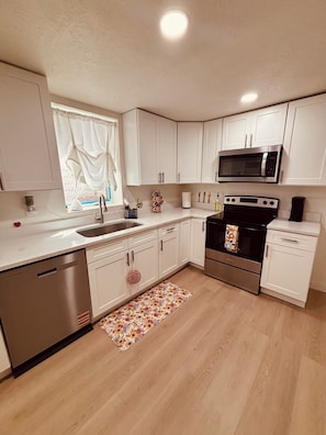 Una cocina moderna con armarios blancos, electrodomésticos de acero inoxidable, lavavajillas y una alfombra con motivos florales.