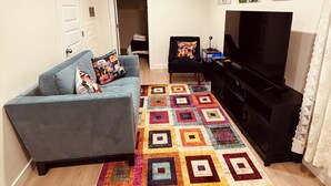 A living room with a blue sofa, a black entertainment unit, a colorful rug, and a TV. - Basement Cozy Corner Be one of the first to stay in this comfortable space! (Salt Lake City)