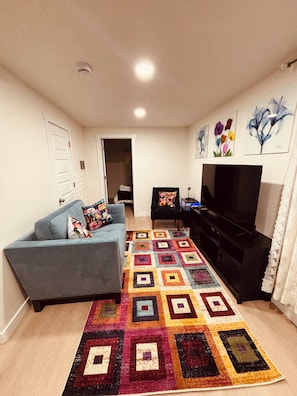 Una sala de estar con un sofá azul, un mueble multimedia negro, un tapete colorido y un televisor.