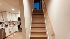 A staircase leading to an upper floor, a kitchen area with white cabinets, and a wooden floor. - Basement Cozy Corner Be one of the first to stay in this comfortable space! (Salt Lake City)