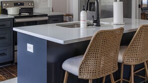 A modern kitchen with a central island, stainless steel appliances, and wicker bar stools. - Near Benning, Steps to Riverwalk/Bibb Mill, 2 Kings, Queen Sofa Bed, Sleeps 6 (Columbus)