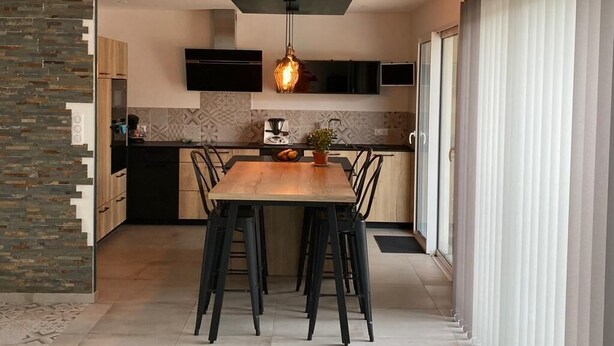 Una cocina moderna con comedor, que incluye una mesa de madera, sillas negras y una lámpara colgante.