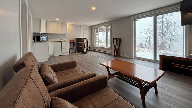 A spacious living area with a sofa set, a dining table, and a kitchen in the background.