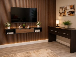 Ein modernes Wohnzimmer mit an der Holzwand montiertem Fernseher, einem Konsolentisch mit Dekorationsobjekten und einem Sofa.