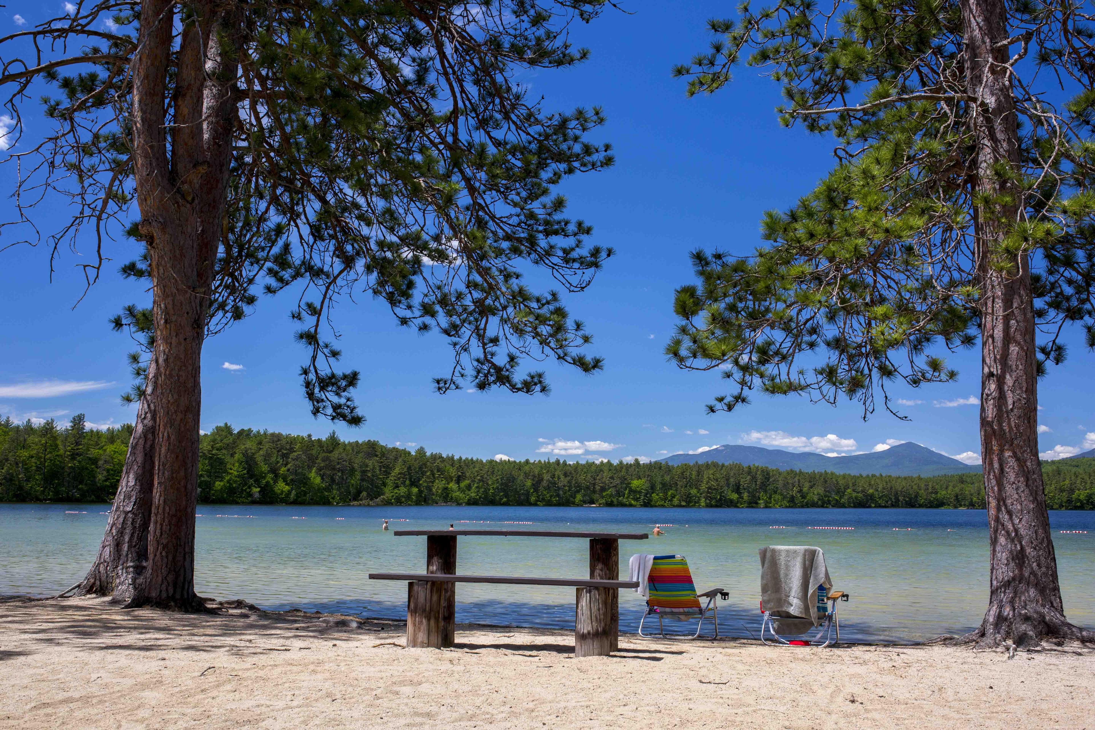 A lakeside setting with a wooden bench and a beach chair near the water.