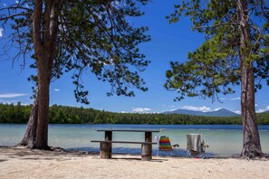 A lakeside setting with a wooden bench and a beach chair near the water.