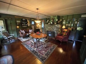 Een eetgedeelte met een ronde tafel, stoelen, een vloerkleed, een open haard en een boekenkast.