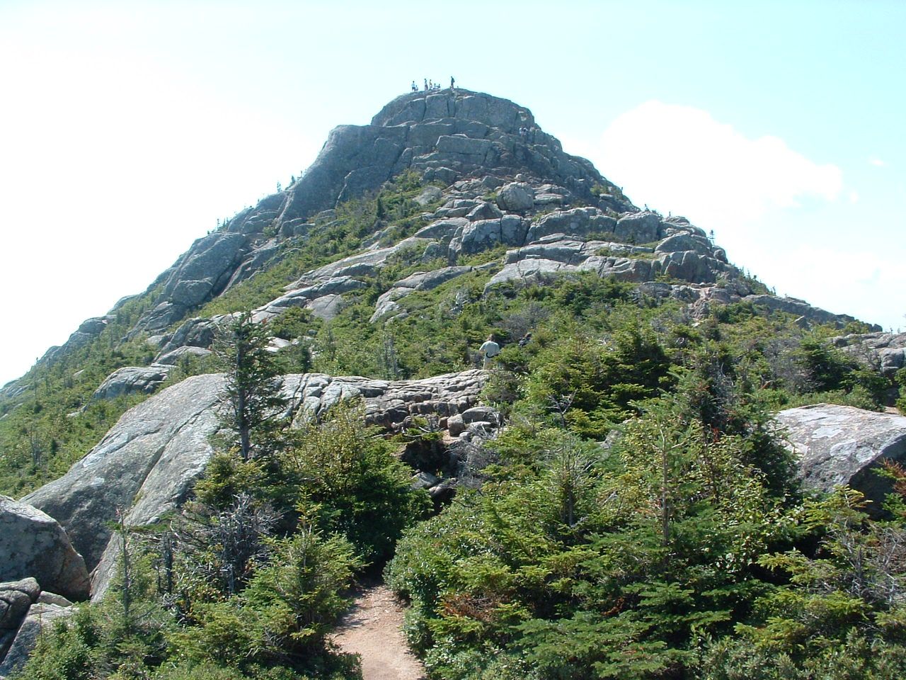 A mountain with a rocky path leading to its peak, surrounded by dense vegetation.