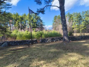 A stone wall, a flagpole with a flag, and a tree in a natural setting.