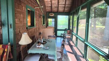 A wooden interior with a dining table, chairs, and a view through large windows.