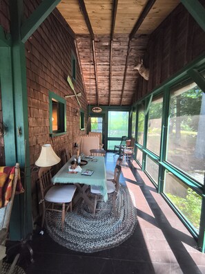 A wooden interior with a dining table, chairs, and a view through large windows.