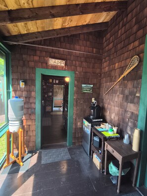 A rustic interior with a brick wall, a sign reading 'LAMP,' a water dispenser, a coffee machine, and a table with cups and utensils.