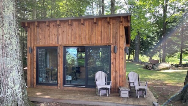 Una cabaña de madera con grandes puertas de vidrio, dos sillas Adirondack y una terraza.