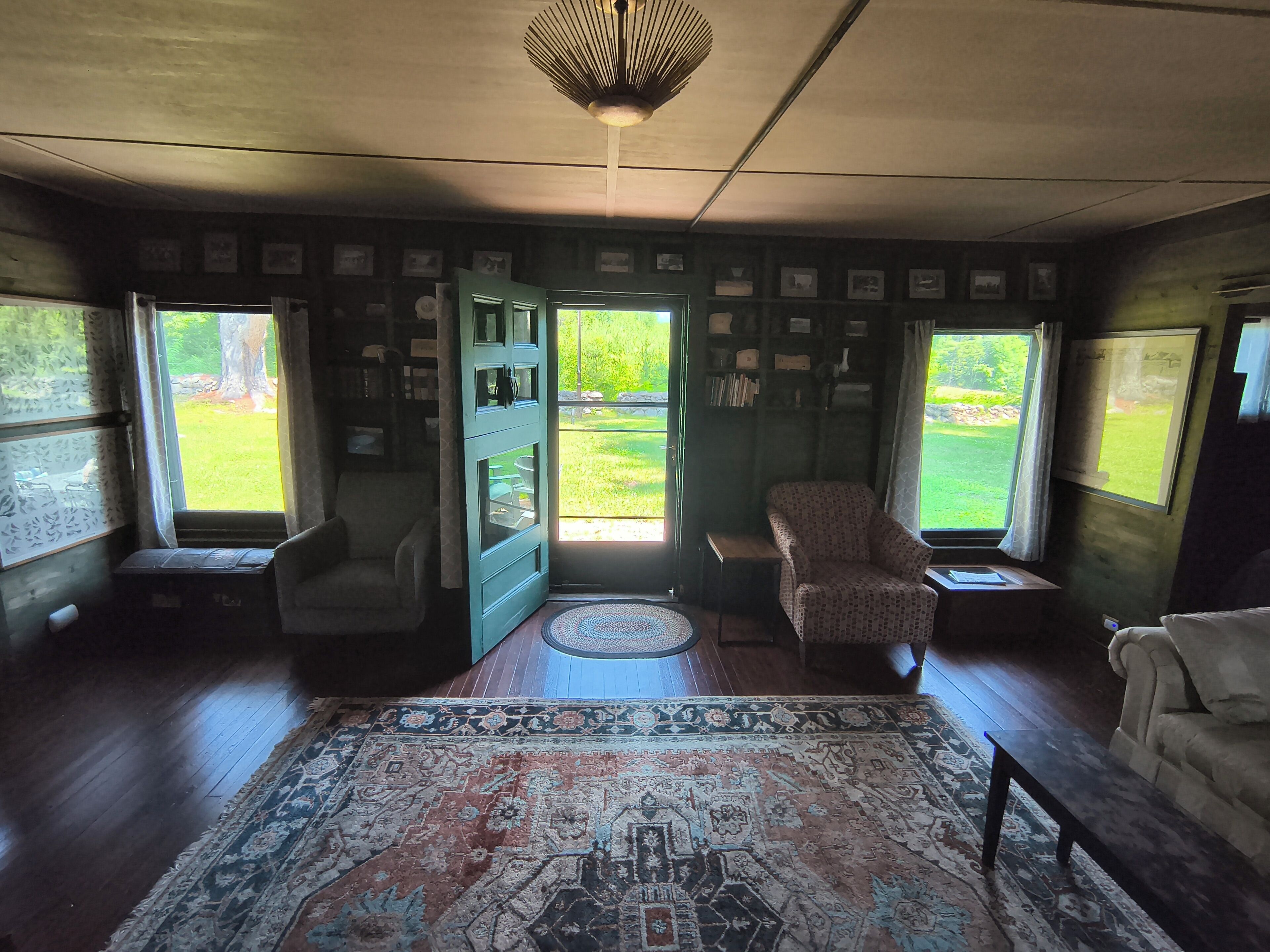 A room with a large rug, two chairs, a small table, and a door leading outside.