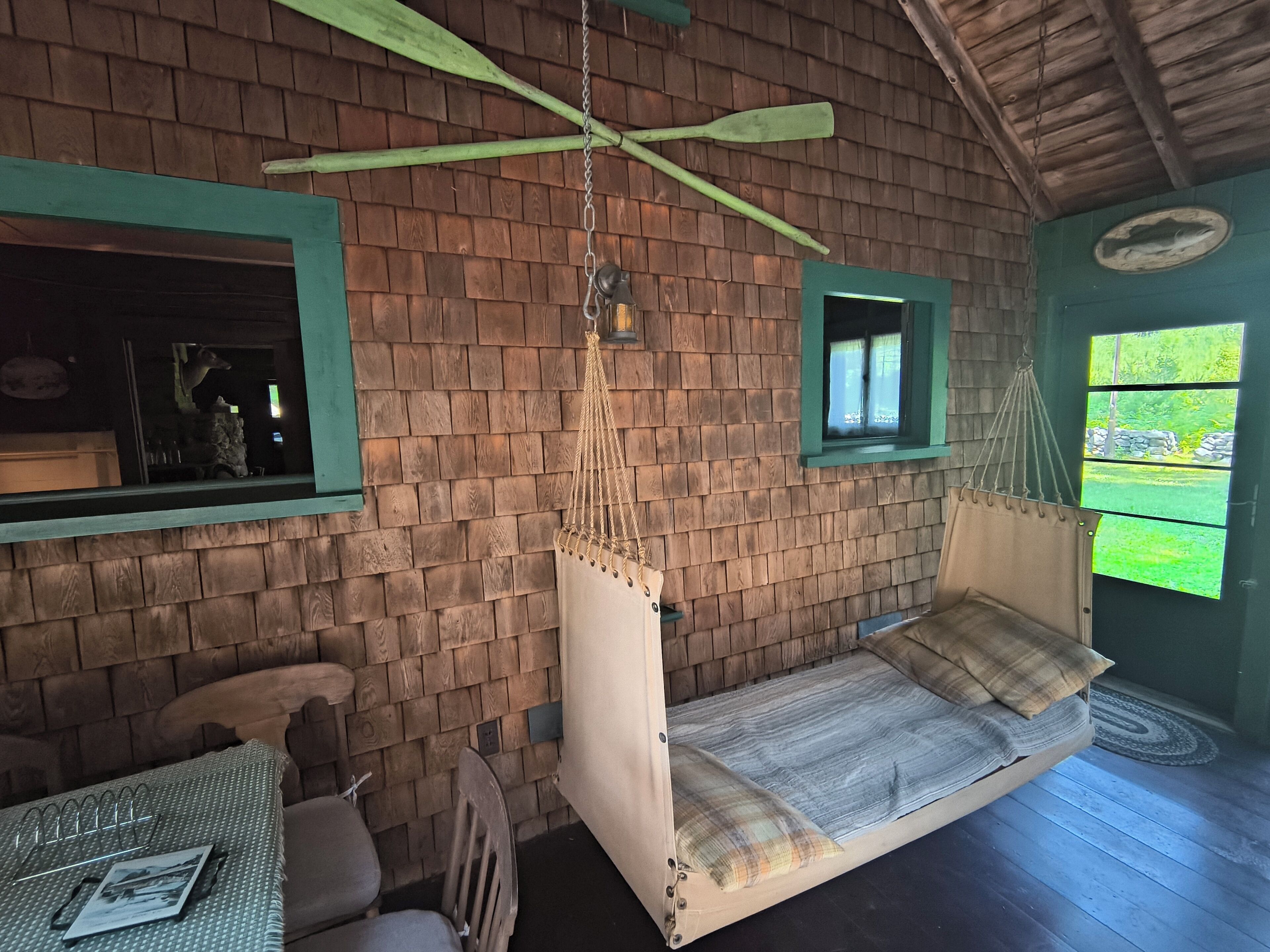 Una habitación rústica con pared de ladrillo y madera, una hamaca colgante, una mesita con una silla y una ventana con vistas a la vegetación.
