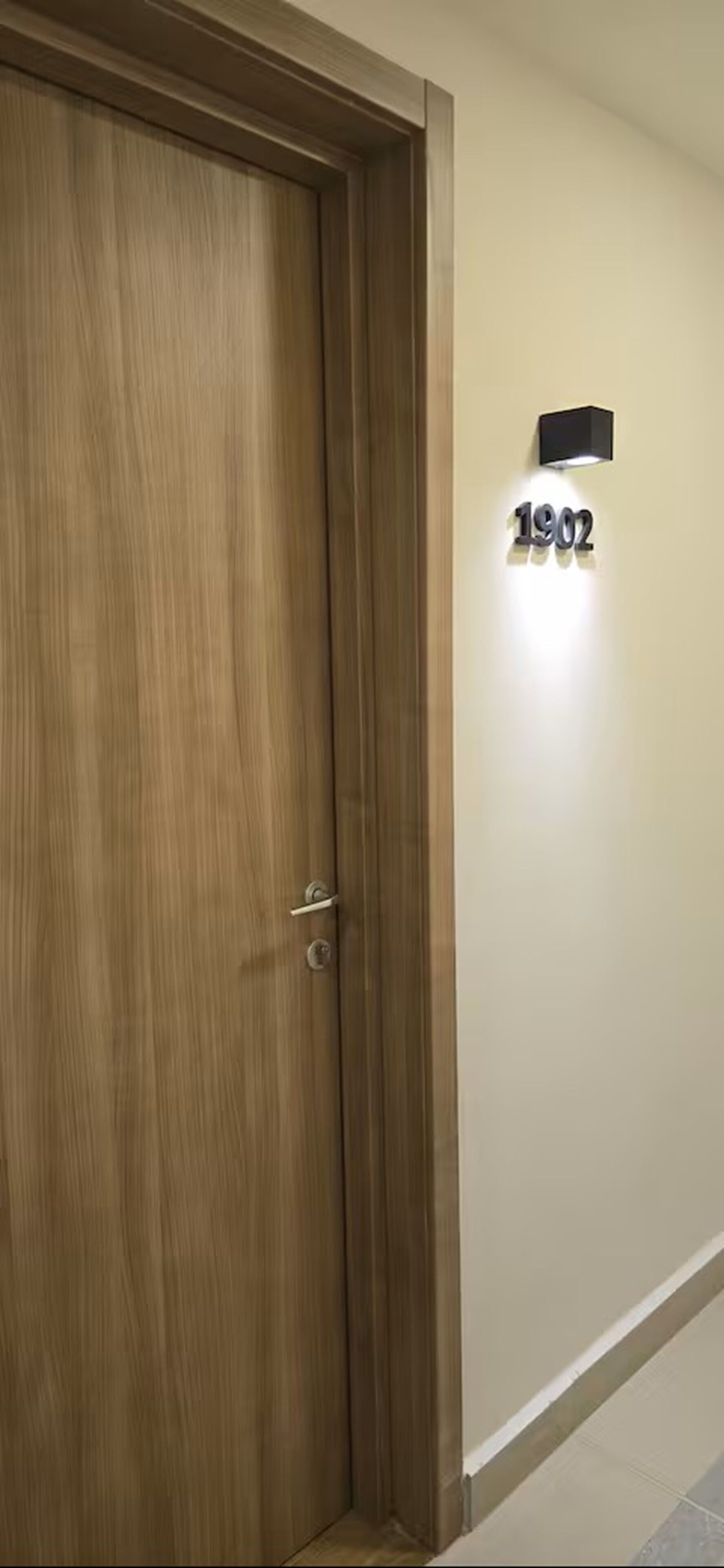 Une porte en bois avec une poignée en métal, un luminaire fixé au mur et une plaque portant le numéro « 1902 ».