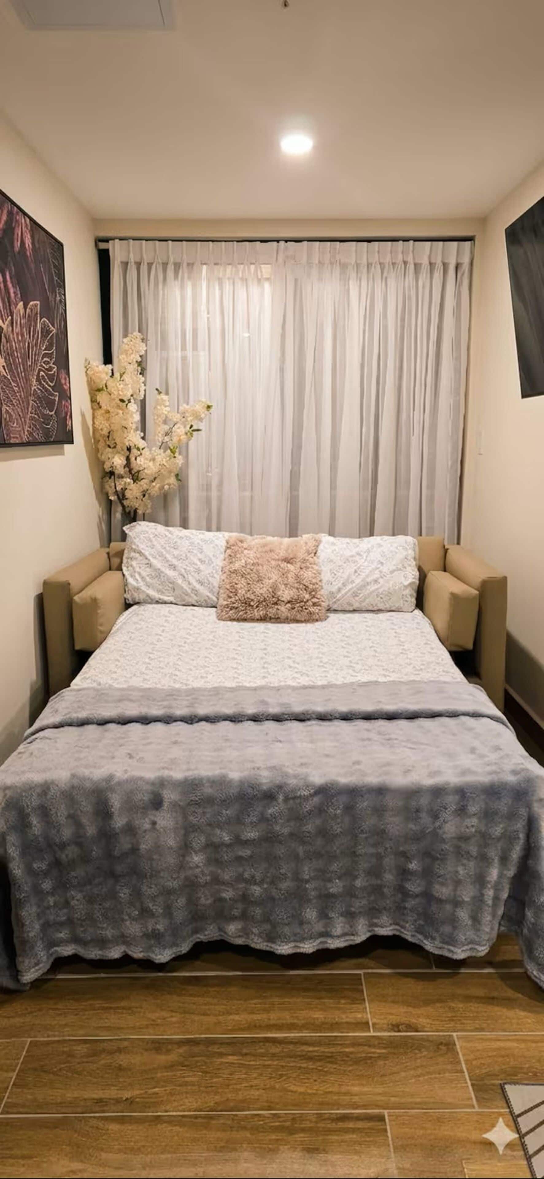 A bedroom with a bed, curtains, a vase of flowers, and a painting on the wall.